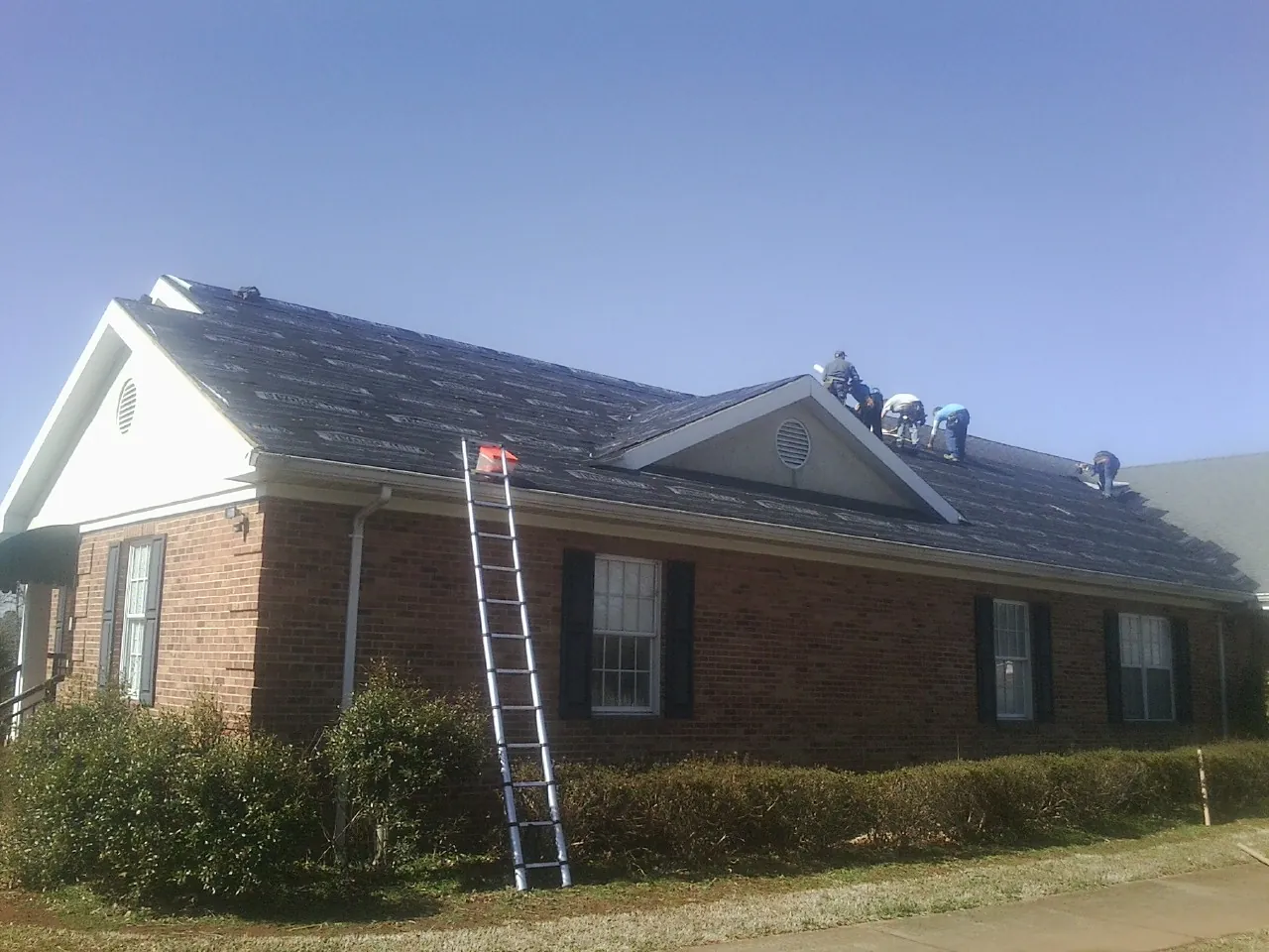 Crew tearing shingles off a brick ranch roof with a ladder set — Metal Roof Repair work by our crew in Rossville