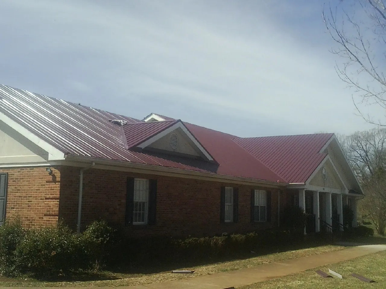 Red metal roof with gabled entries on a long brick building, from a Hail Damage Roof Repair job in Rossville