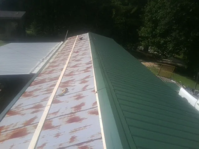 Old rusted panels beside newly installed green metal roofing — Wind Damage Roof Repair by Roofing Brothers in Rossville