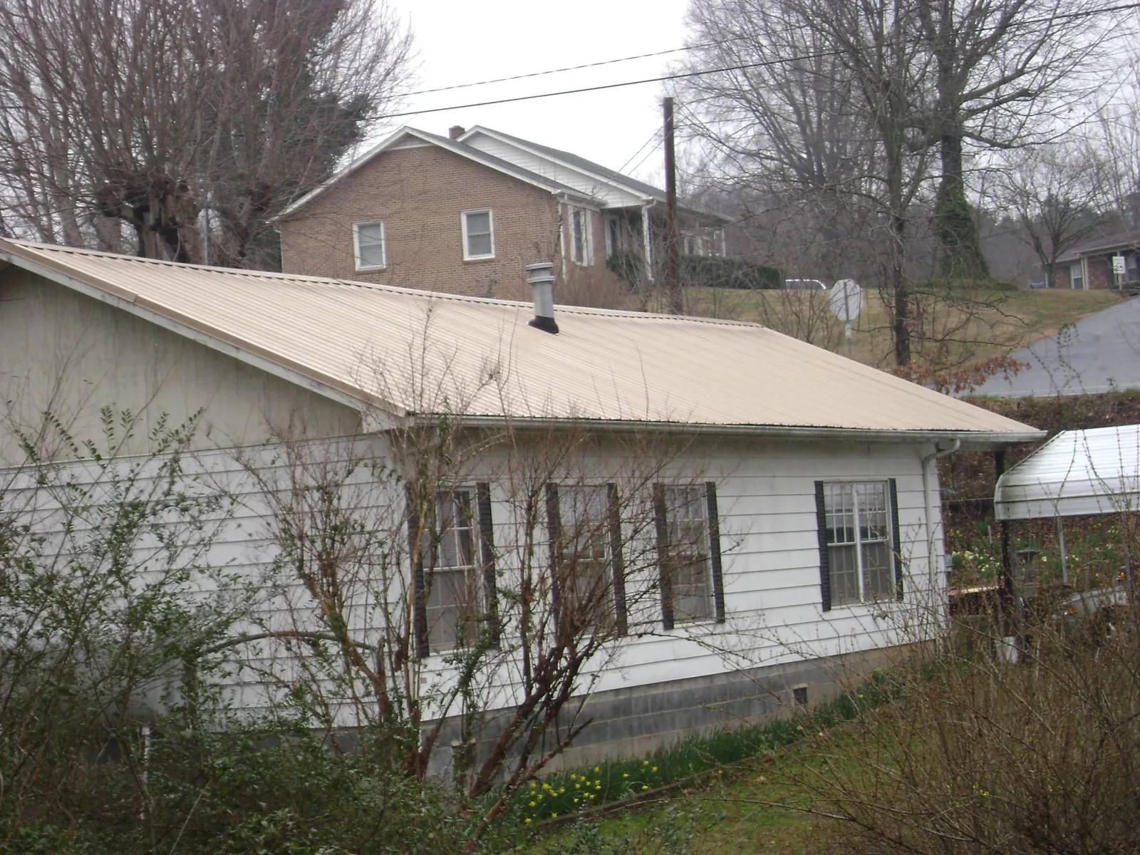 Tan metal roof on a white sided house set into a hillside — Commercial Roofing by Roofing Brothers in Rossville
